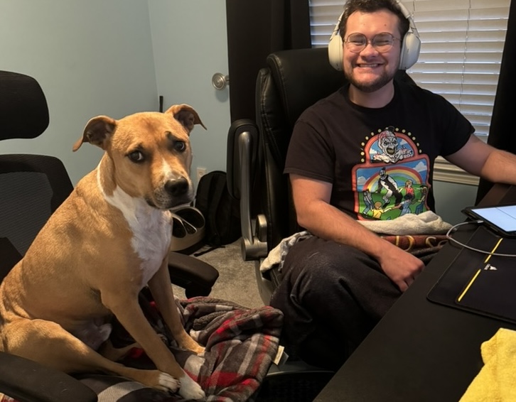 Greg working on the computer while his dog sits next to him in a chair